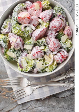 Salad of broccoli, strawberries, red onion and almonds dressed with yogurt close-up in a plate. Vertical top view 113421274
