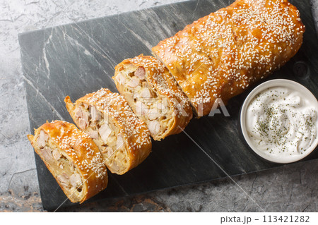 Homemade strudel with chicken, mushrooms and cheese served with sauce close-up on a board. Horizontal top view Homemade strudel with chicken, mushrooms and cheese served with sauce close-up on a board. Horizontal top view 113421282