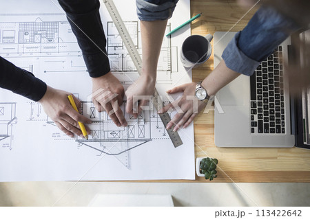 High angle view of worker's hand working on blueprint over wooden table at workplace High angle view of worker's hand working on blueprint over wooden table at workplace 113422642