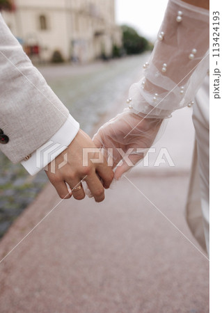 Close-up of groom holds bride's hand. Wedding couple walking in the centre of the city Close-up of groom holds bride's hand. Wedding couple walking in the centre of the city 113424193