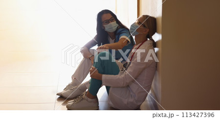 Surgeon in hospital corridor with communicates with doctor sitting on floor 113427396