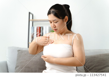 Asian woman checking lumps on her breast for signs of breast cancer by her self at home. Asian woman checking lumps on her breast for signs of breast cancer by her self at home. 113427541