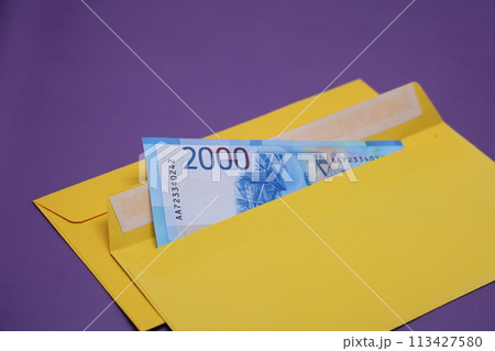 Banknotes in a yellow envelope on a purple background. Bribery concept. Salary in envelopes, fraud. Banknotes in a yellow envelope on a purple background. Bribery concept. Salary in envelopes, fraud. 113427580