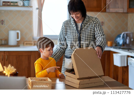 Grandmother and grandson are standing at the table and opening a box of pizza. Generation connection concept. 113427776