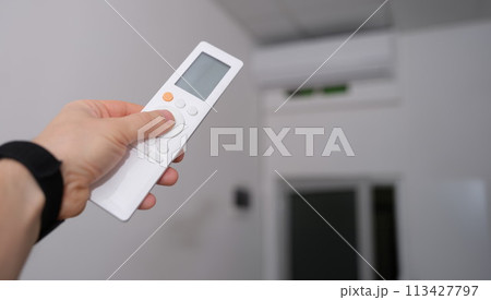 Hand with remote control is directed to air conditioner in room Hand with remote control is directed to air conditioner in room 113427797