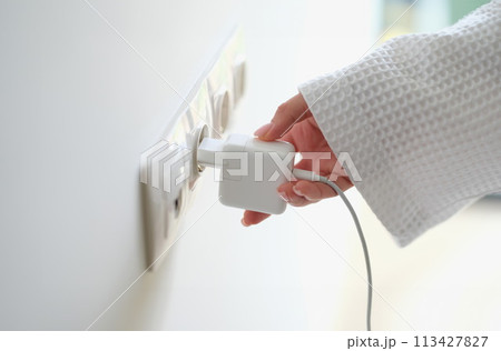 Woman hand in robe gown inserts white charger into socket in hotel rooms or at home 113427827