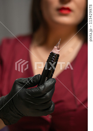 girl holds a tattoo machine in her hands near her face 113429978