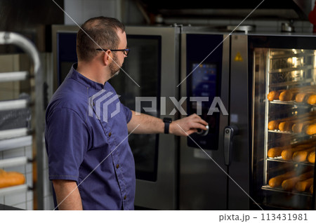 Baker in kitchen near oven with baguettes in bakehouse Baker in kitchen near oven with baguettes in bakehouse 113431981