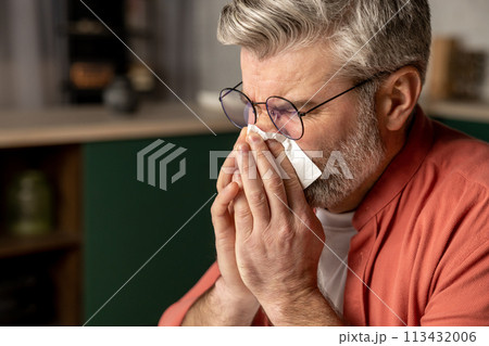 Sick middle aged grey haired man with fever and runny nose using handkerchief 113432006