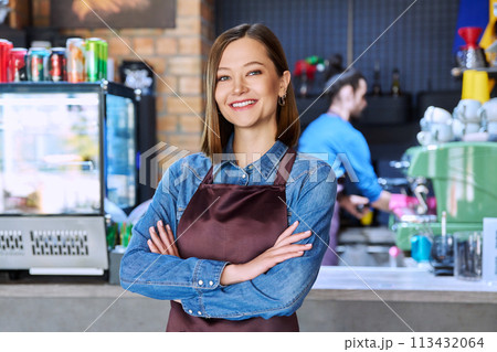 Young woman service worker in apron looking at camera in restaurant, coffee shop 113432064