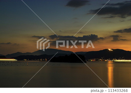 夕焼けの瀬戸内に灯る万葉火とフェリーの光跡 113433268
