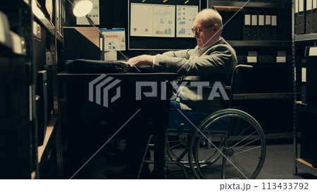 Paralyzed senior inspector reviewing classified case records in incident room, gathering intelligence for private investigation. Wheelchair user with limited mobility accessing databases. Camera B. 113433792