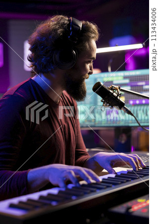 Sound engineer playing piano keyboard to compose new music, singing on microphone and adding audio effects in post production. Artist composer creating songs for music industry. Sound engineer playing piano keyboard to compose new music, singing on microphone and adding audio effects in post production. Artist composer creating songs for music industry. 113434006