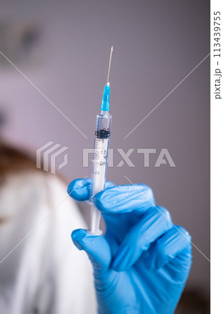 Close-up of a syringe with liquid in the hand of a doctor of a woman in a blue glove 113439755
