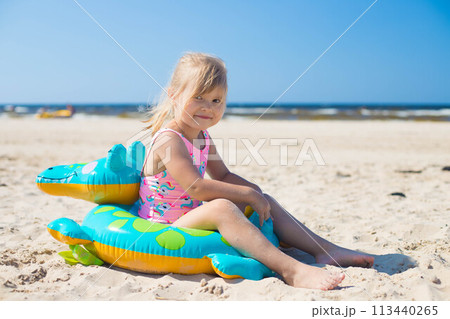 Happy girl sitting on an inflatable crocodile toy at the beach sunny day 113440265