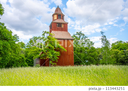 Seglora Church rustic red wooden facade stands out against the lush greenery on a bright summer day in Stockholm open-air museum, Skansen. Sweden Seglora Church rustic red wooden facade stands out against the lush greenery on a bright summer day in Stockholm open-air museum, Skansen. Sweden 113443251