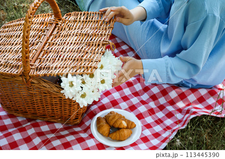 A girl on a picnic with a wicker basket and croissants A girl on a picnic with a wicker basket and croissants 113445390
