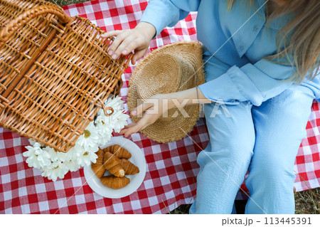 A girl on a picnic with a wicker basket and croissants A girl on a picnic with a wicker basket and croissants 113445391