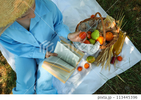 A girl in a straw hat is reading a book on a picnic A girl in a straw hat is reading a book on a picnic 113445396