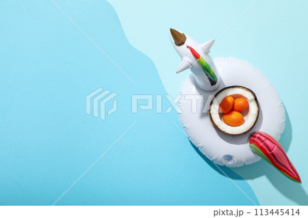 Inflatable ring for swimming and kumquat in half coconut on blue background, space for text 113445414