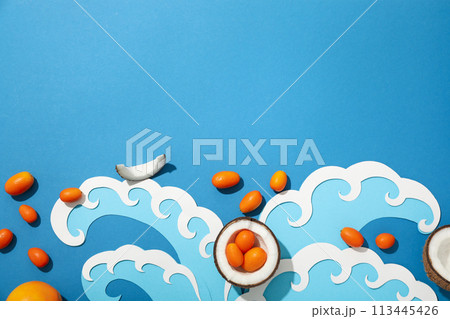 Pieces of coconut, whole kumquats and paper waves on blue background, space for text Pieces of coconut, whole kumquats and paper waves on blue background, space for text 113445426