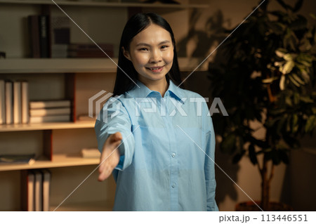 Young Asian Woman in Blue Shirt Waving Hello in a Modern Office Setting 113446551