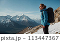 A young happy European woman with a tourist backpack stands on top of a rock in the mountains, travels and enjoys a beautiful view of the mountains, sky or nature. Untouched nature. Tourism and travel 113447367
