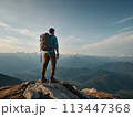 A young happy European man a tourist backpack stands on top of a rock in the mountains, travels and enjoys a beautiful view of the mountains, sky or nature. Untouched nature. Tourism and travel 113447368