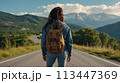 Young positive African American woman with a tourist backpack stands on top of a rock in the mountains, travels and enjoys a beautiful view of the mountains, sky or nature. Untouched nature. Tourism 113447369