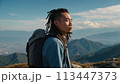 A young happy Chinese man with a tourist backpack stands on top of a rock in the mountains, travels and enjoys a beautiful view of the mountains, sky or nature. Untouched nature. Tourism and travel 113447373