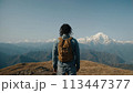 A young happy Chinese man with a tourist backpack stands on top of a rock in the mountains, travels and enjoys a beautiful view of the mountains, sky or nature. Untouched nature. Tourism and travel 113447377