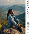 Young positive African American woman with a tourist backpack stands on top of a rock in the mountains, travels and enjoys a beautiful view of the mountains, sky or nature. Untouched nature. Tourism 113447388
