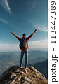 A young happy European man a tourist backpack stands on top of a rock in the mountains, travels and enjoys a beautiful view of the mountains, sky or nature. Untouched nature. Tourism and travel 113447389