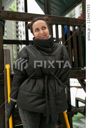 Weekend concept, a young woman with a bun hairstyle walks on a playground with a swing in the yard 113447555