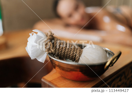 Ayurvedic treatment Kizhi from Kerala, effective rejuvenation treatment. Closeup selective focus shot of Ayurveda massage powder pads on blurred background of lying female client in wellness salon. 113449427