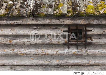 Old wooden house roof with green moss and wall made of rough gray logs Old wooden house roof with green moss and wall made of rough gray logs 113451380