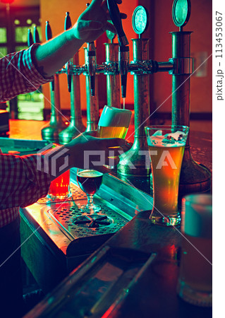 Beer culture. Bartender's hands pouring lager foamy beer from the taps with precision and care in mugs 113453067