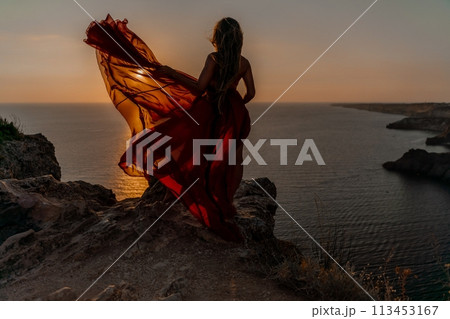 Woman sunset sea red dress, side view a happy beautiful sensual woman in a red long dress posing on a rock high above the sea on sunset. 113453167