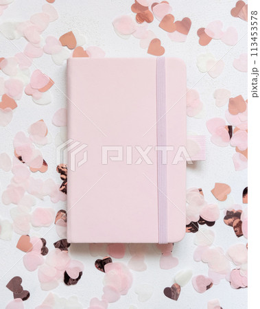 Pink hardcover notebook between pink hearts on white table top view, textbook mockup 113453578