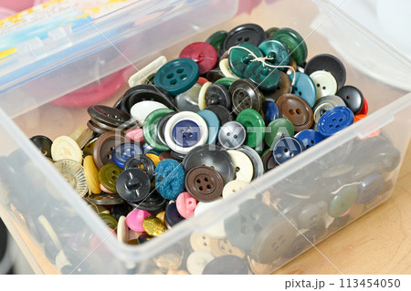 An assortment of colorful buttons in a clear plastic container with a white background 113454050