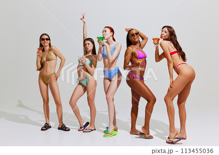 Women wearing colorful bikinis, with sunglasses posing with playful expression against white background. 113455036