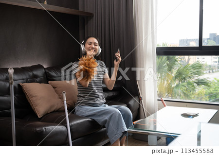 Cheerful young woman having fun cleaning house, singing and using duster as microphone Cheerful young woman having fun cleaning house, singing and using duster as microphone 113455588