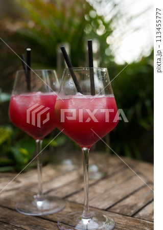 Red cocktail with ice in glass with stem on wooden surface Red cocktail with ice in glass with stem on wooden surface 113455777