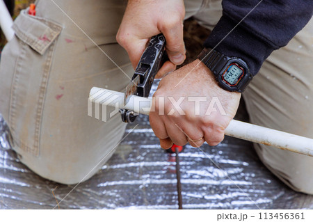 Technician plumber cuts a plastic PVC pipe by special scissors 113456361
