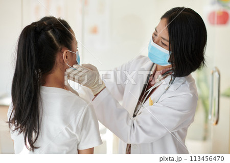 Pediatrician palpating neck lymph nodes of teenage girl 113456470