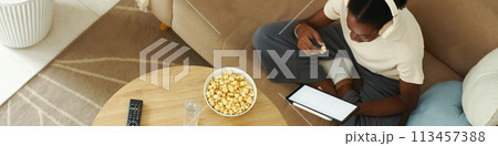 Header with Black girl eating popcorn and reading article on tablet computer 113457388