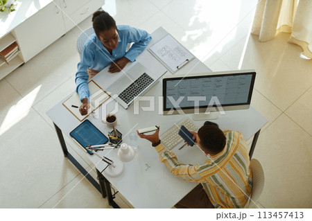 Young entrepreneur showing notepad with ideas for project development to colleague Young entrepreneur showing notepad with ideas for project development to colleague 113457413