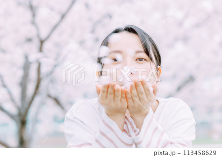 桜の花びらを吹く若い女性 113458629