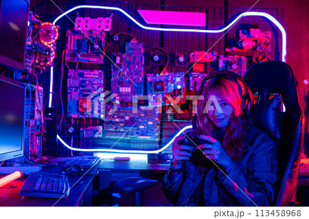 Gamer using joystick controller for virtual tournament plays online video game with computer neon lights, woman wear gaming headphones playing live stream esports games console at home 113458968
