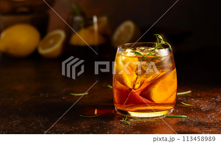 Iced tea or cocktail with ice, rosemary and lemon slices on the old brown table. 113458989